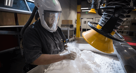 a 3D printing technician removes nylon powder from an SLS part